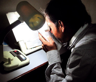 Man reading with a magnifier and lamp