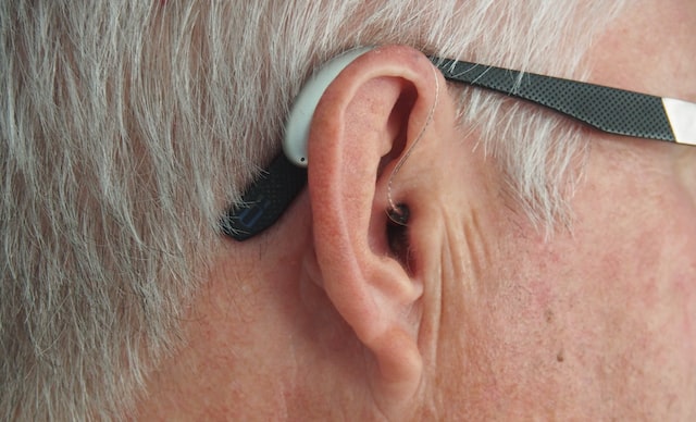 Profile of a person with gray hair wearing glasses and a hearing aid