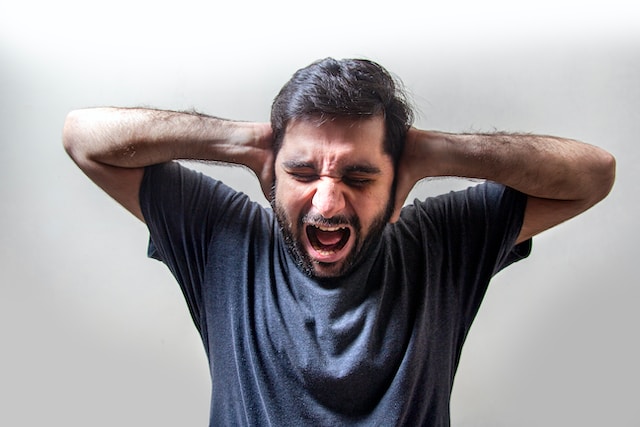 Man holding his hands to his ears with his mouth open in frustration