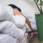 A person in bed with arm hanging off and a plant next to them