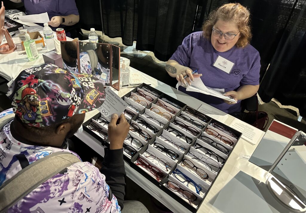 Mission of Mercy volunteer helping a man choose eyeglasses