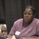 A woman trying eyeglasses at Mission of Mercy as a volunteer looks on