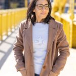 Virginia Montanez wearing a white sweater and tan coat on a yellow Pitt bridge