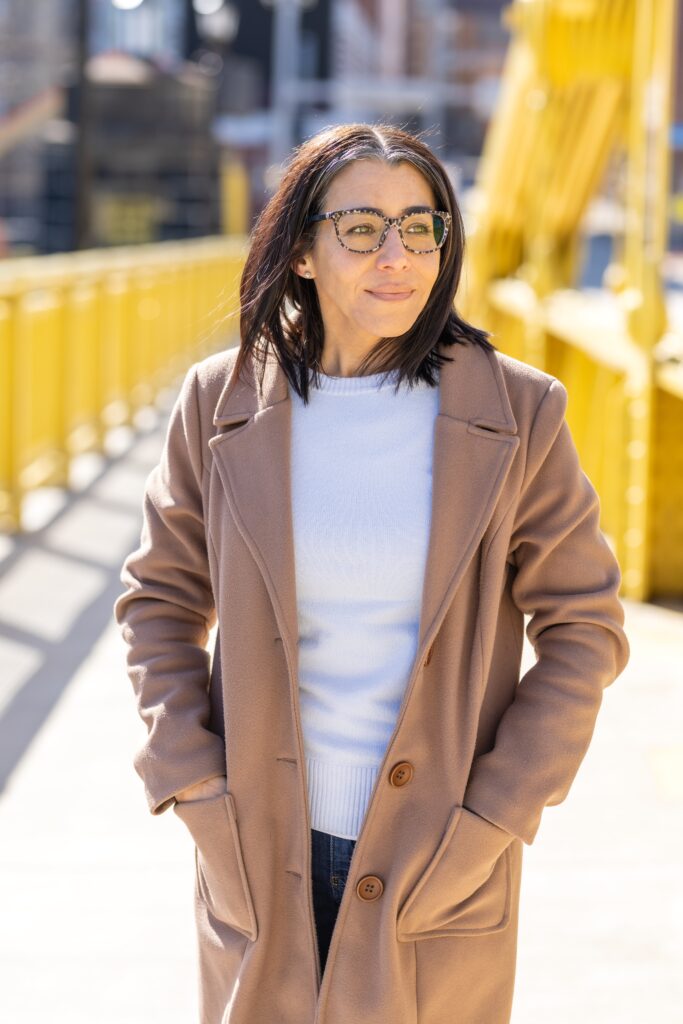 Virginia Montanez wearing a white sweater and tan coat on a yellow Pitt bridge