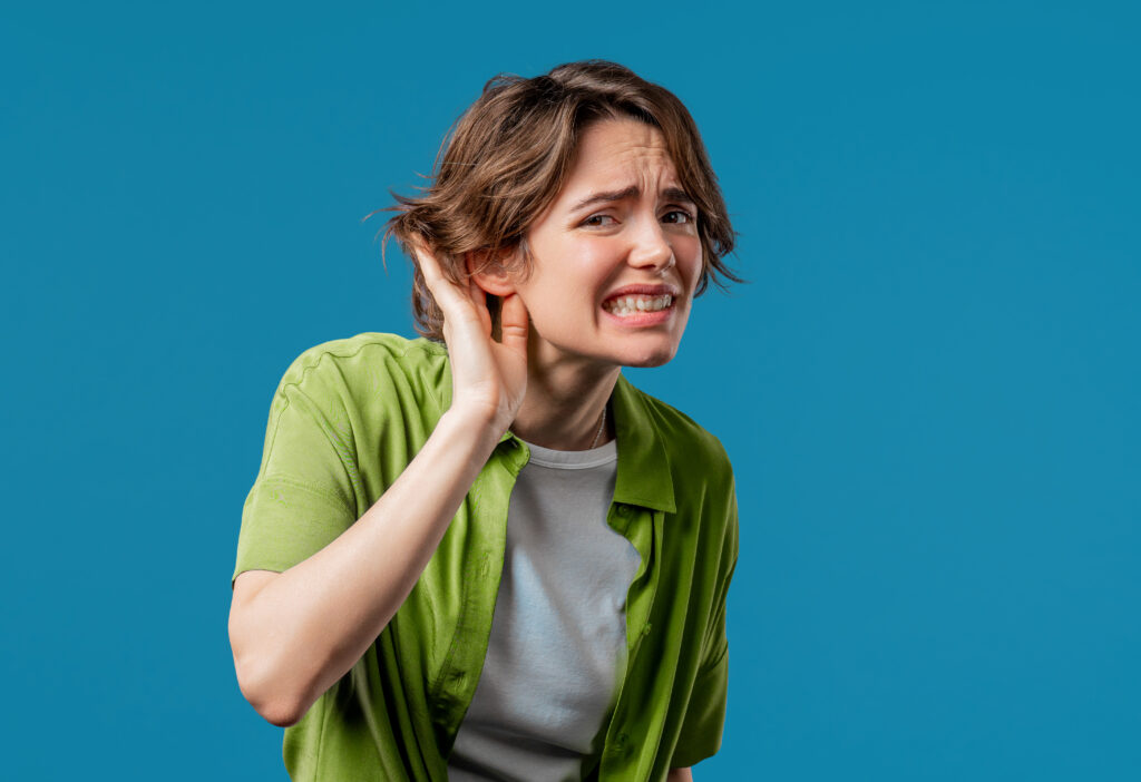 Woman cupping her ear, clearly not hearing, in front of a blue background
