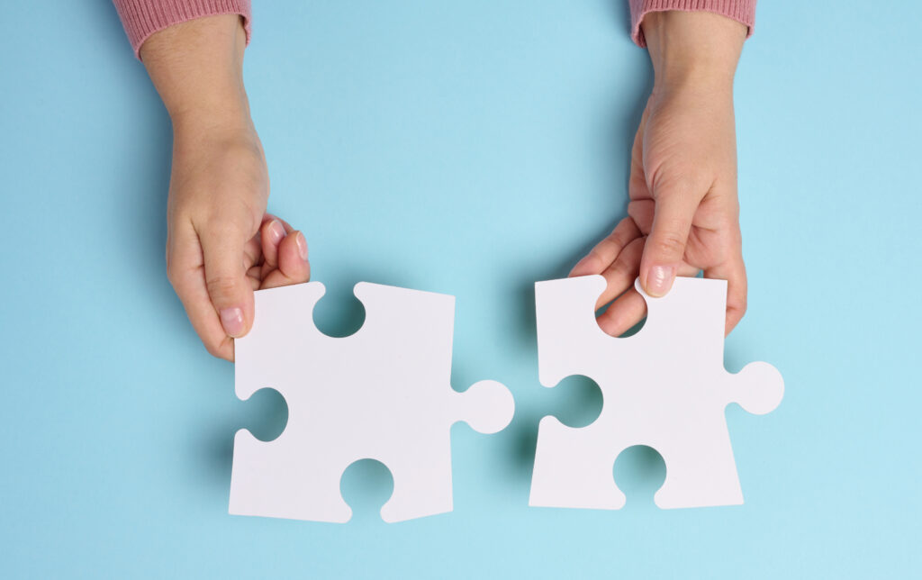 Female hand holds two large paper empty white jigsaw puzzles on a blue background, top view