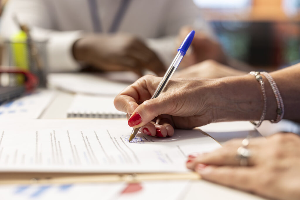 Elderly woman giving her signature on retirement plan contract, choosing the suitable pension option with life insurance policy to secure the future income and family expenses. Close up.