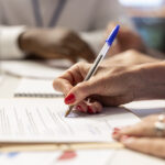 Elderly woman giving her signature on retirement plan contract, choosing the suitable pension option with life insurance policy to secure the future income and family expenses. Close up.
