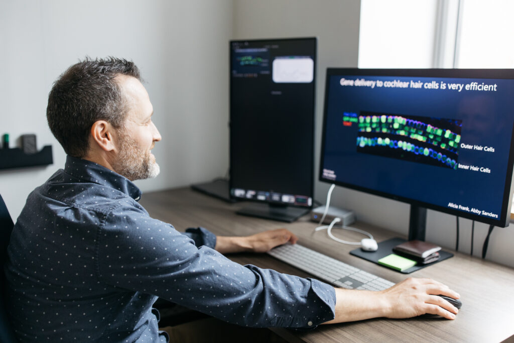 Chris Cunningham at his computer, which has a slide that reads, "Gene delivery to cochlear hair cells is very efficient."