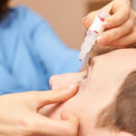 Ophthalmologist applying eye drops by holding patient's eye open