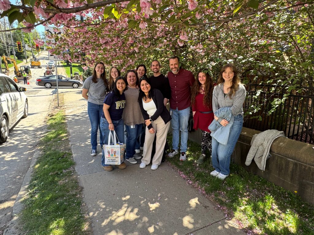 The Cunningham Lab in a group photo taken outside on a sidewalk by some flowering trees