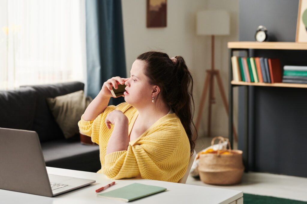 woman with Down syndrome on phone with a laptop in front of her